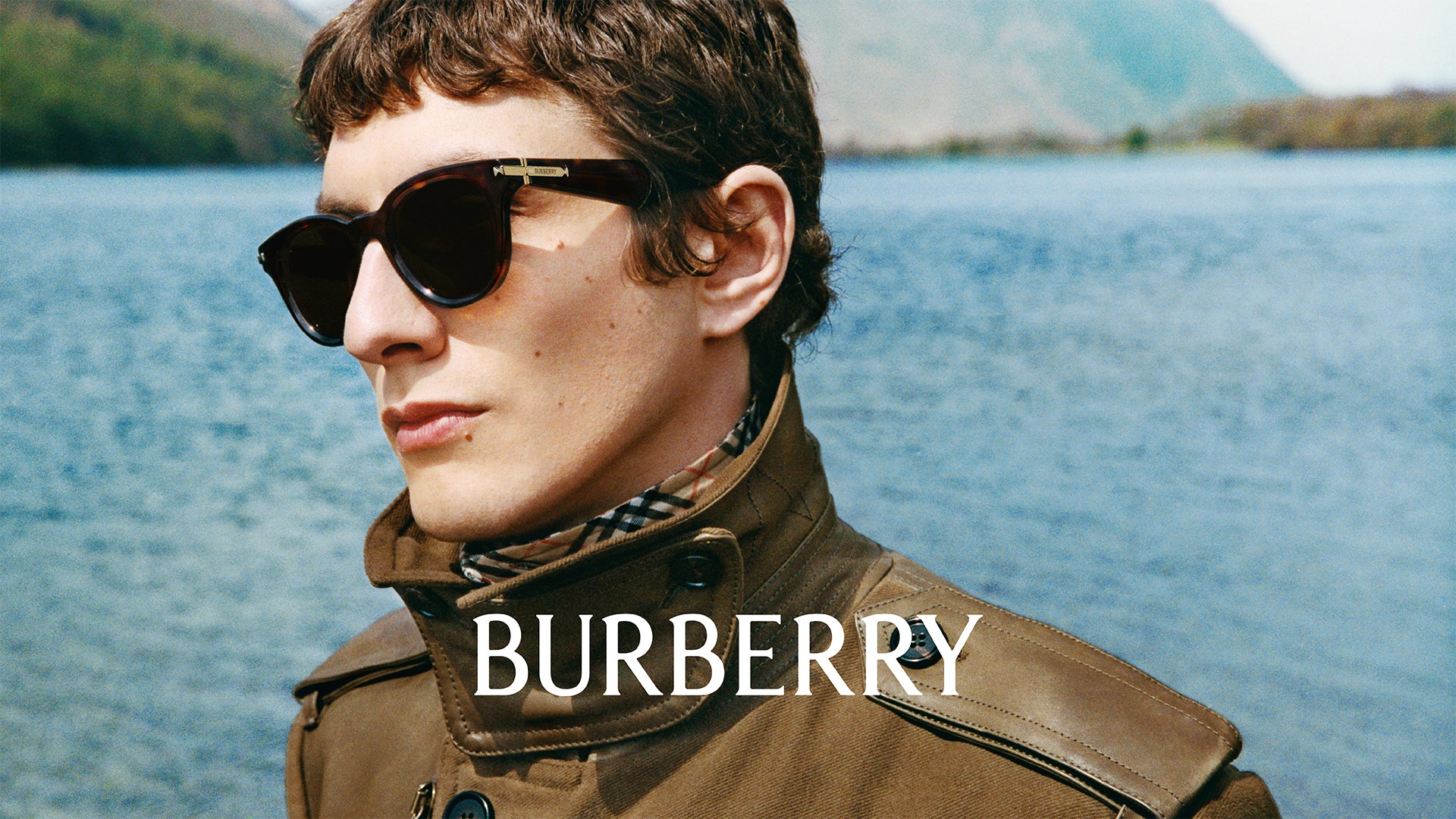 Man wearing sunglasses and a Burberry jacket with a lake in the background