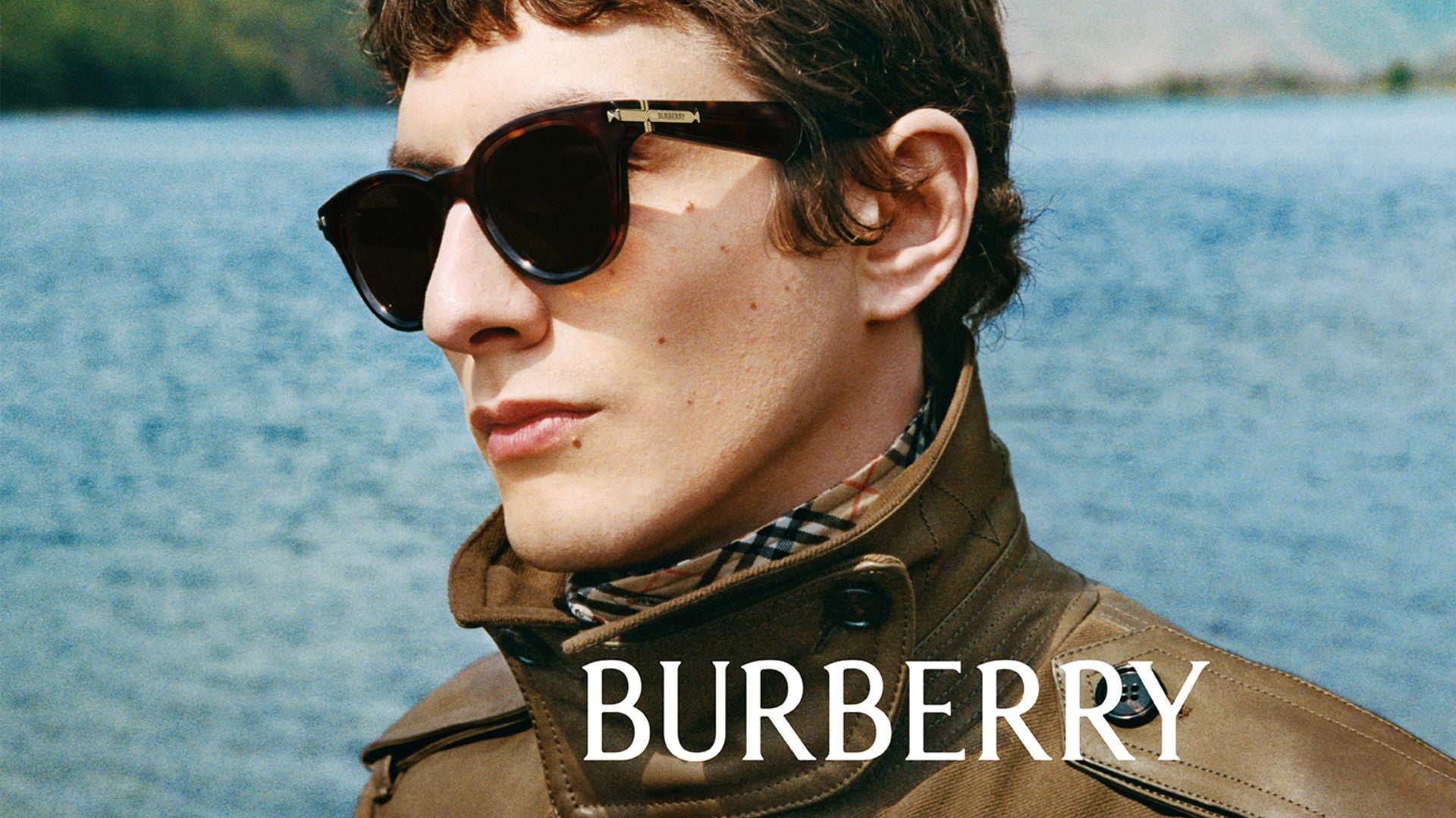 Man wearing sunglasses and a Burberry jacket with a blurred natural background
